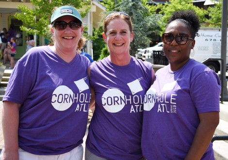 Three ladies wearing Cornhole ATL t-shirts and smiling
